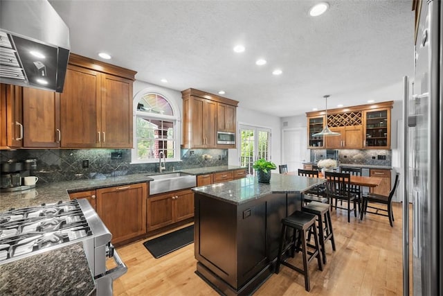116 Bunker Hill Dr, Peters Twp, PA 15317 - kitchen featuring wall chimney exhaust hood, appliances with stainless steel finishes, backsplash, light wood finished floors, and brown cabinetry