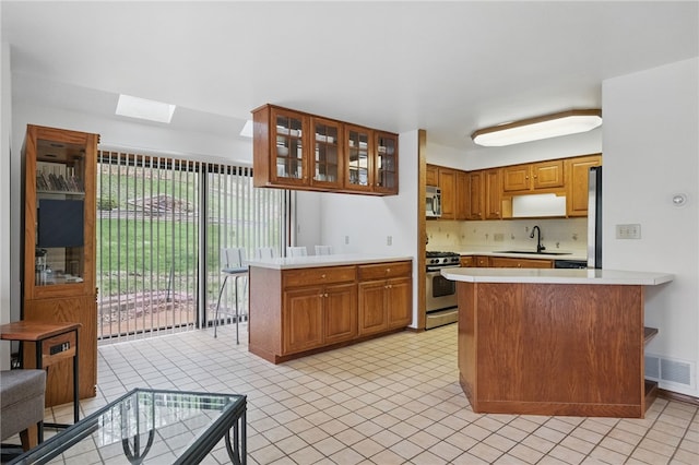 1 Quail Hill Rd, Fox Chapel, PA 15238 - kitchen with appliances with stainless steel finishes, a peninsula, light countertops, a skylight, and brown cabinets