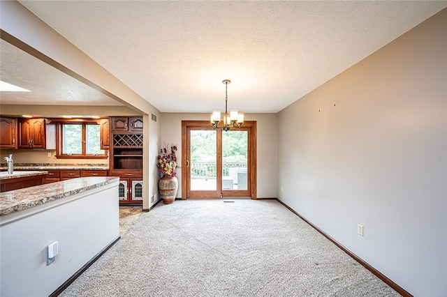 317 Bridlewood Dr, Hempfield Twp Wml, PA 15601 - kitchen with light carpet, a chandelier, plenty of natural light, brown cabinets, and a textured ceiling