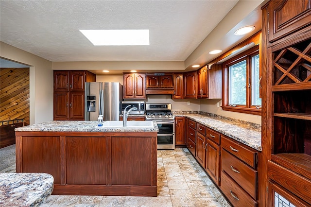 317 Bridlewood Dr, Hempfield Twp Wml, PA 15601 - kitchen with stainless steel appliances, under cabinet range hood, a skylight, a center island with sink, and light stone finish flooring