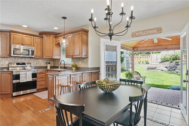 3236 Beacon Hill Ave, Dormont, PA 15216 - kitchen featuring appliances with stainless steel finishes, a chandelier, decorative backsplash, dark countertops, and brown cabinetry