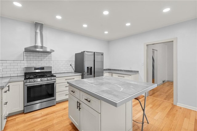 841 Stanton Ave, Millvale, PA 15209 - kitchen featuring appliances with stainless steel finishes, wall chimney range hood, white cabinets, light wood-style flooring, and a breakfast bar