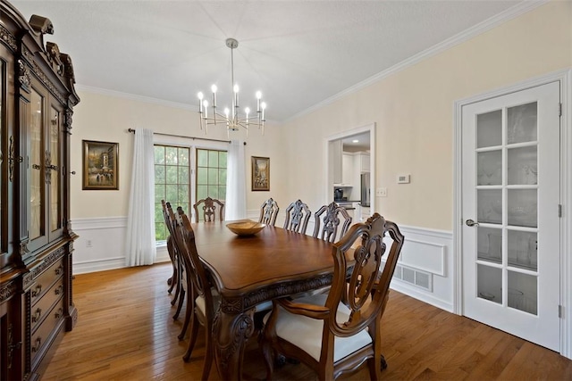 7052 Bennington Woods Dr, Mccandless, PA 15237 - dining room featuring a chandelier, ornamental molding, light wood-style flooring, wainscoting, and a decorative wall