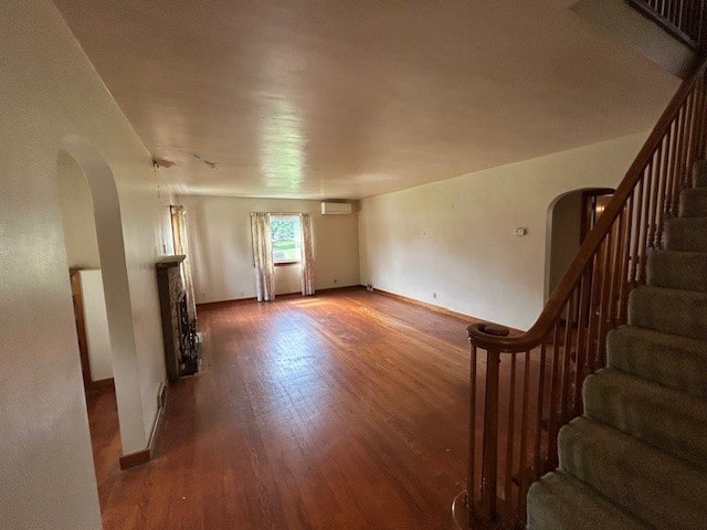 300 6th Ave, New Eagle, PA 15067 - unfurnished living room featuring arched walkways, wood finished floors, stairway, and an AC wall unit
