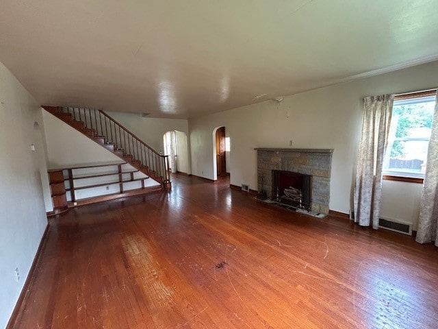 300 6th Ave, New Eagle, PA 15067 - unfurnished living room featuring hardwood / wood-style floors, arched walkways, a stone fireplace, and stairs