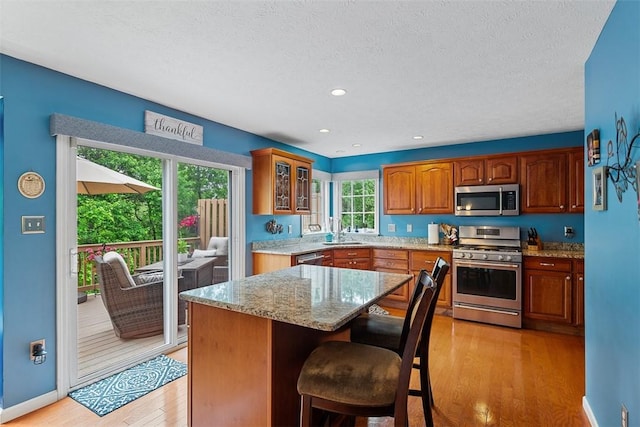 81406 Lost Valley Dr, Adams Twp, PA 16046 - kitchen featuring appliances with stainless steel finishes, glass insert cabinets, light stone counters, light wood finished floors, and a kitchen island