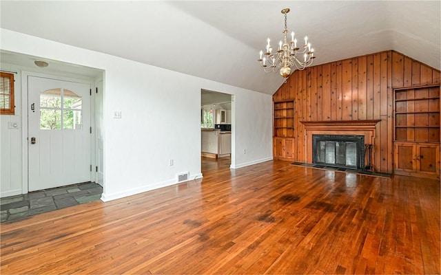 300 S Pasadena Dr, Fox Chapel, PA 15215 - unfurnished living room featuring lofted ceiling, a chandelier, hardwood / wood-style floors, wood walls, and a glass covered fireplace