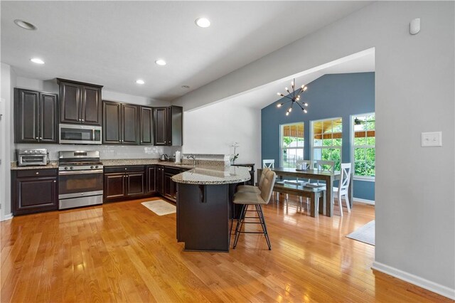 265 Sunrise Dr, Collier Twp, PA 15106 - kitchen featuring stainless steel appliances, lofted ceiling, a peninsula, a breakfast bar area, and light wood-style flooring