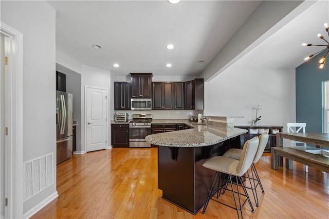 265 Sunrise Dr, Collier Twp, PA 15106 - kitchen featuring stainless steel appliances, a peninsula, a kitchen breakfast bar, light stone countertops, and light wood finished floors