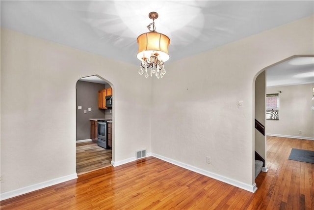 129 Temona Dr, Pleasant Hills, PA 15236 - empty room with arched walkways, light wood-style floors, and a chandelier