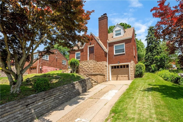 129 Temona Dr, Pleasant Hills, PA 15236 - tudor home featuring concrete driveway, a chimney, an attached garage, a front lawn, and brick siding