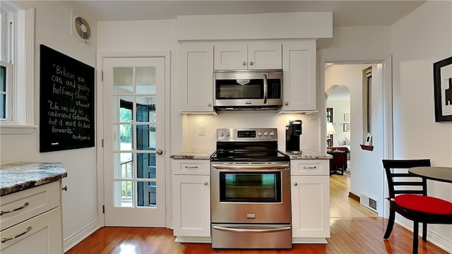217 Monroe Dr, Ross Twp, PA 15229 - kitchen with stainless steel appliances, light wood finished floors, arched walkways, light stone countertops, and white cabinets