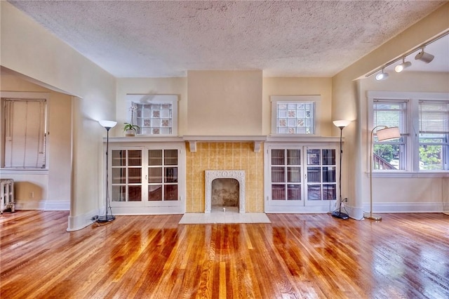 2267 Tilbury Ave, Squirrel Hill, PA 15217 - unfurnished living room featuring wood finished floors, a tiled fireplace, radiator, healthy amount of natural light, and a textured ceiling