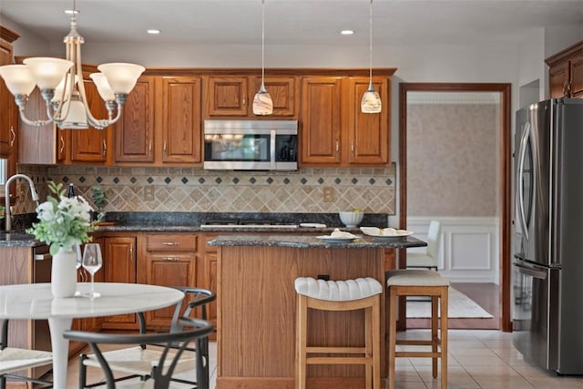 105 Averys Way, Cranberry Twp, PA 16066 - kitchen with stainless steel appliances, a kitchen island, brown cabinets, light tile patterned floors, and wainscoting