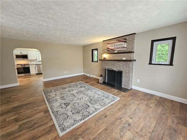 946 Herman Rd, Summit Twp But, PA 16002 - unfurnished living room with a textured ceiling, dark wood-type flooring, a brick fireplace, and arched walkways