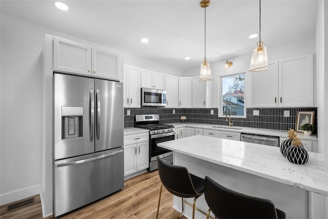 141 Blackhawk St, Squirrel Hill, PA 15218 - kitchen featuring appliances with stainless steel finishes, tasteful backsplash, white cabinetry, a breakfast bar, and light stone counters
