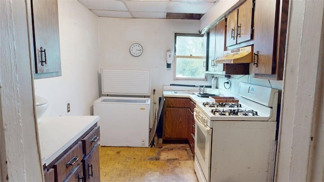 237 Wick St, Hill District, PA 15219 - kitchen featuring white gas stove, under cabinet range hood, brown cabinets, light countertops, and a paneled ceiling