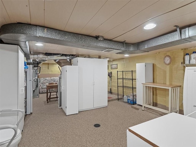 finished basement with concrete block wall, recessed lighting, and freestanding refrigerator