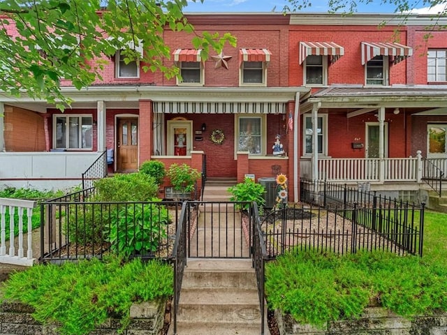 multi unit property featuring covered porch, stairway, brick siding, and a fenced front yard