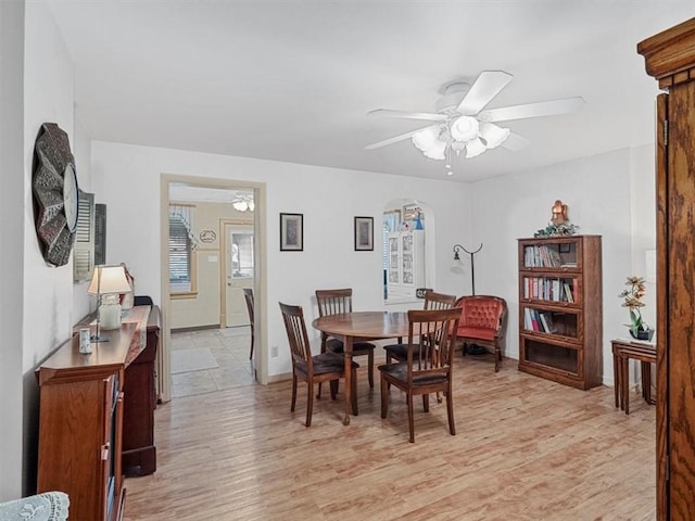 dining space with a ceiling fan, arched walkways, and light wood-type flooring