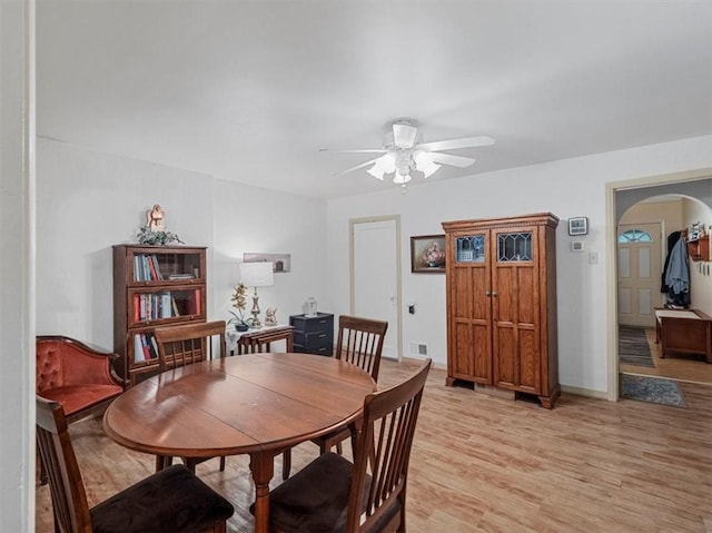 dining space with arched walkways, ceiling fan, and light wood-style flooring
