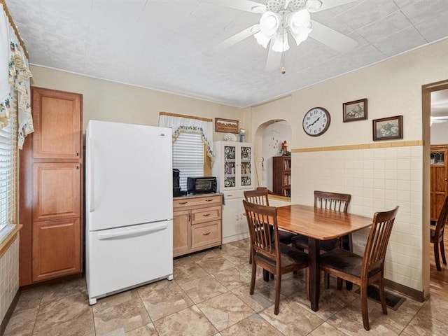 dining space with arched walkways, a ceiling fan, healthy amount of natural light, and tile walls