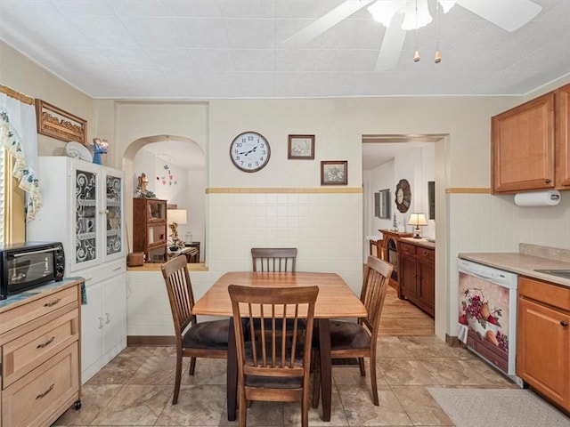 dining space featuring tile walls, a ceiling fan, and arched walkways