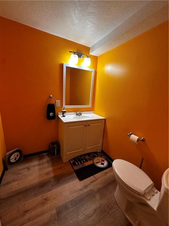 half bath with a textured ceiling, wood finished floors, and vanity