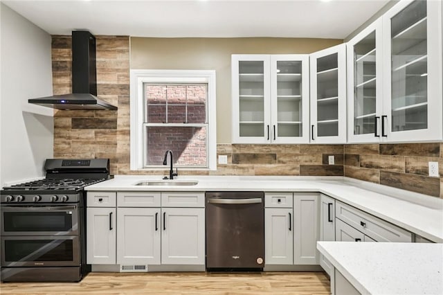 515 Peebles St, Wilkinsburg, PA 15221 - kitchen with appliances with stainless steel finishes, wall chimney exhaust hood, tasteful backsplash, light wood-type flooring, and glass insert cabinets