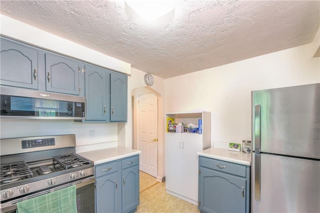 2688 Summit St, Bethel Park, PA 15102 - kitchen featuring stainless steel appliances, light countertops, a textured ceiling, blue cabinetry, and arched walkways