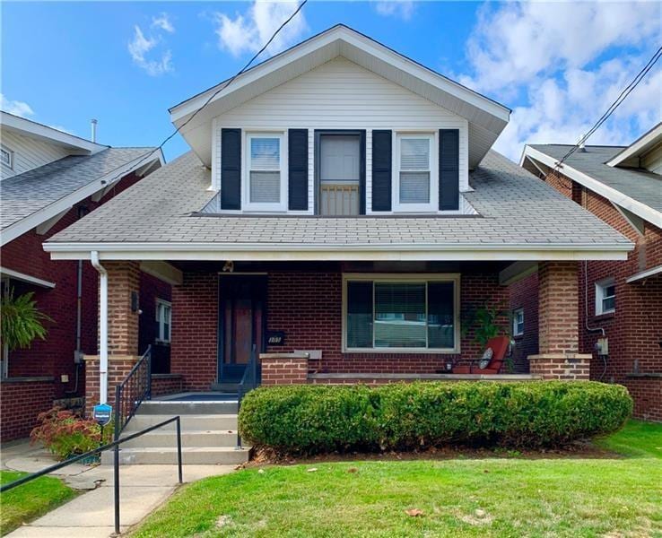 305 5th Ave, New Kensington, PA 15068 - view of front of house with covered porch, brick siding, a front lawn, and roof with shingles