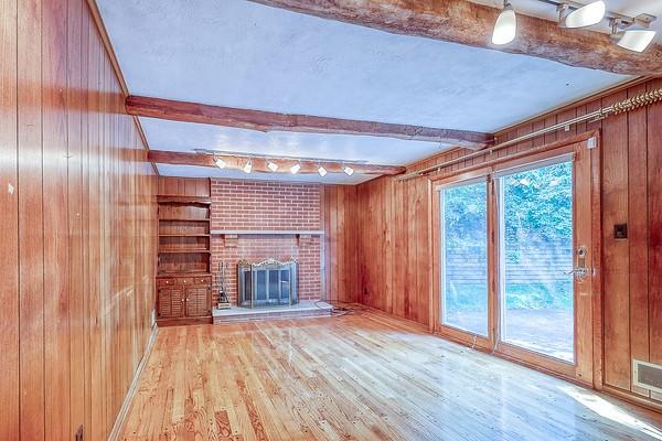 4517 W Brightview Ave, Whitehall, PA 15227 - unfurnished living room with beamed ceiling, wooden walls, wood finished floors, and a brick fireplace