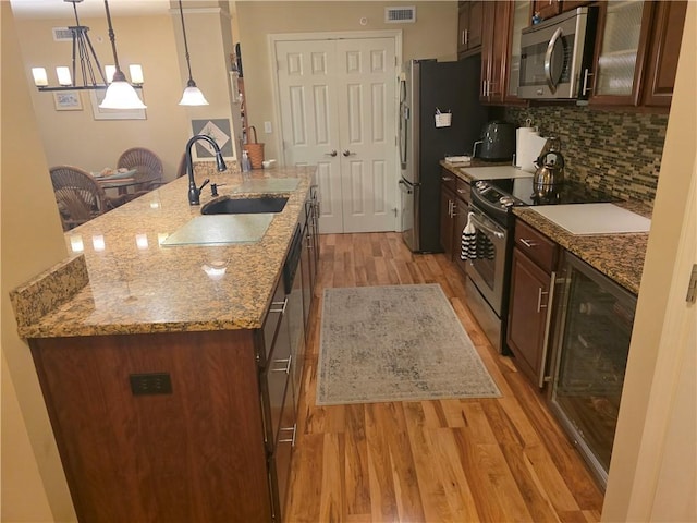7007 Stefano Dr, Delmont, PA 15626 - kitchen featuring appliances with stainless steel finishes, light wood-style flooring, an island with sink, decorative backsplash, and glass insert cabinets