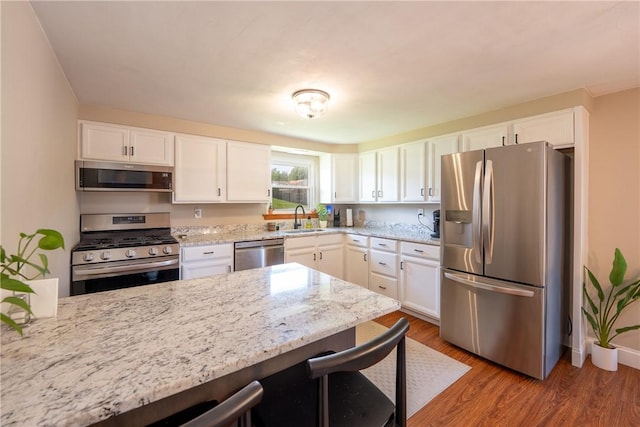 205 Eleanor Dr, Latrobe, PA 15650 - kitchen with stainless steel appliances, a kitchen breakfast bar, white cabinets, light stone counters, and wood finished floors