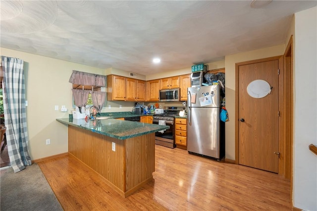 318 Links Ct, Salem Twp Wml, PA 15626 - kitchen featuring appliances with stainless steel finishes, a peninsula, dark countertops, light wood-style floors, and brown cabinetry