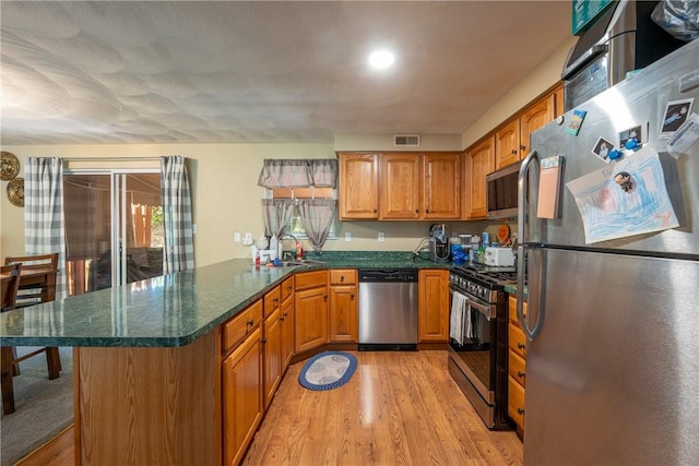 318 Links Ct, Salem Twp Wml, PA 15626 - kitchen with appliances with stainless steel finishes, a peninsula, light wood-style flooring, brown cabinetry, and dark stone countertops