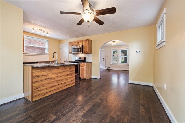 2072 Dartmore St, Overbrook, PA 15210 - kitchen featuring stainless steel appliances, dark wood-style floors, a ceiling fan, arched walkways, and brown cabinetry