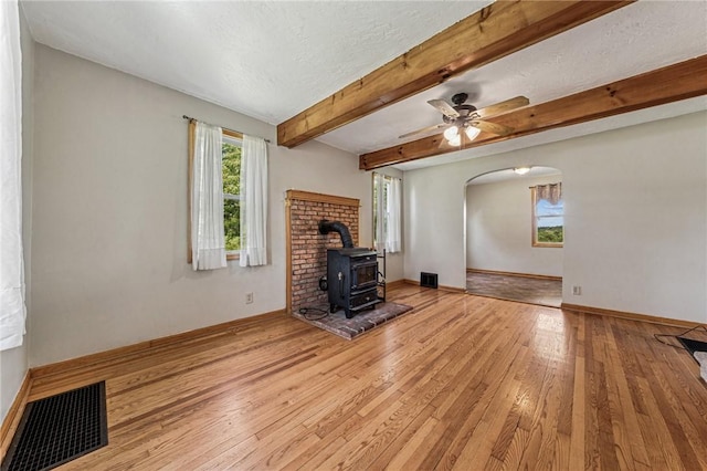 585 Dugan Way, New Kensington, PA 15068 - unfurnished living room featuring a wood stove, light wood-type flooring, arched walkways, a ceiling fan, and beamed ceiling