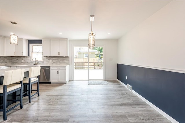 25 Nottingham Dr, Hempfield Twp, PA 15601 - kitchen featuring stainless steel dishwasher, light countertops, white cabinets, tasteful backsplash, and decorative light fixtures