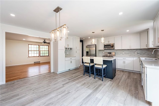 25 Nottingham Dr, Hempfield Twp, PA 15601 - kitchen featuring appliances with stainless steel finishes, decorative backsplash, a kitchen island, light wood-style flooring, and light countertops