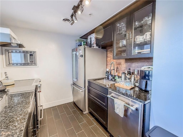 66 Pius St Unit 103, South Side, PA 15203 - kitchen with stainless steel appliances, glass insert cabinets, wall chimney exhaust hood, dark stone countertops, and dark brown cabinetry