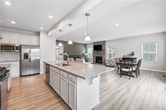 3049 Eagle Ridge Dr, Middlesex Twp, PA 16059 - kitchen featuring stainless steel appliances, a stone fireplace, light wood-style flooring, backsplash, and decorative light fixtures