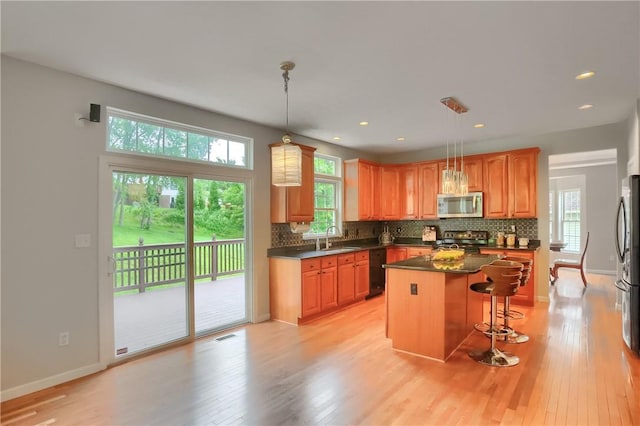 216 Beagle Dr, Moon/Crescent Twp, PA 15108 - kitchen featuring appliances with stainless steel finishes, dark countertops, light wood-type flooring, decorative backsplash, and a kitchen island