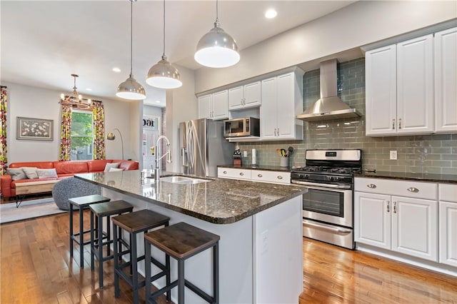 160 45th St, Lawrenceville, PA 15201 - kitchen featuring stainless steel appliances, wall chimney exhaust hood, a breakfast bar area, tasteful backsplash, and light wood finished floors