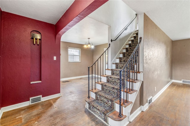 1000 Prospect Rd, Whitehall, PA 15227 - staircase featuring a textured wall, hardwood / wood-style floors, arched walkways, and a chandelier