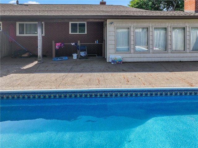 rear view of house with a chimney, a patio area, an outdoor pool, and brick siding