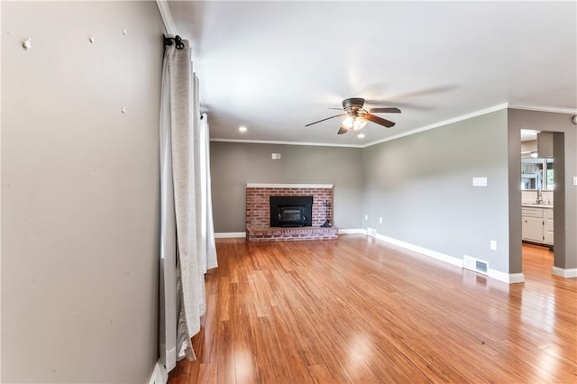 unfurnished living room with ceiling fan, light wood-style floors, a brick fireplace, and crown molding