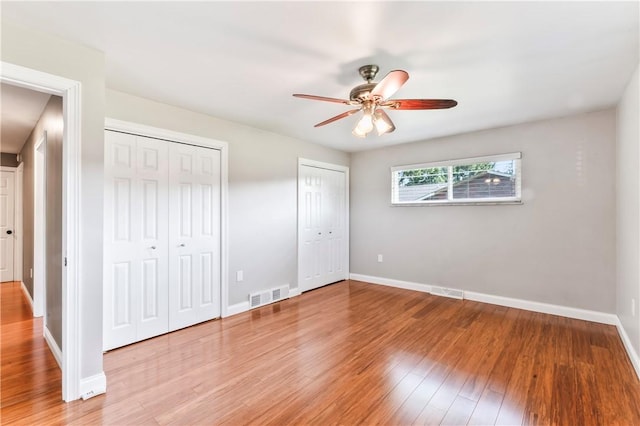 unfurnished bedroom with multiple closets, light wood-style floors, and a ceiling fan