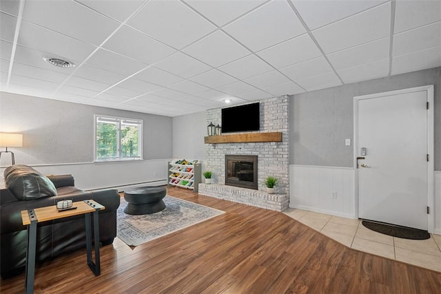 124 Heath Dr, Economy, PA 15005 - living room featuring a drop ceiling, wood finished floors, a wainscoted wall, a brick fireplace, and a baseboard radiator
