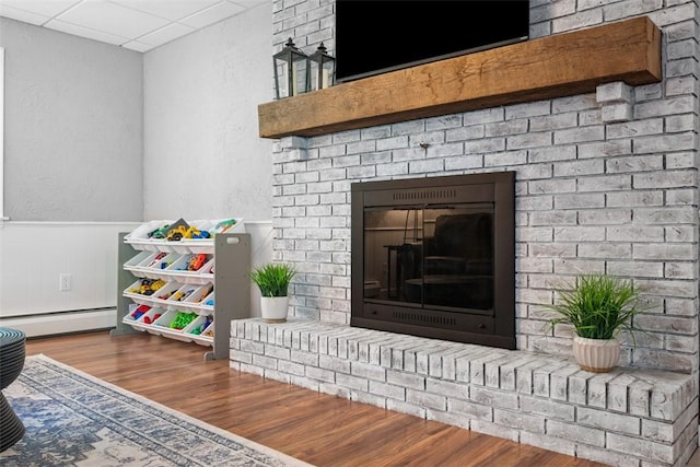 124 Heath Dr, Economy, PA 15005 - detailed view of baseboard heating, a brick fireplace, wood finished floors, a textured wall, and wainscoting